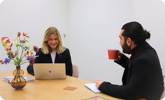 Two colleagues in a meeting discussing work at a table, reflecting personal consultation and support during pricing and plan selection.