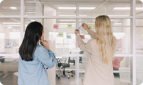 Two colleagues collaborating on content strategy using notes on a glass wall, supporting informed pricing and plan decisions.